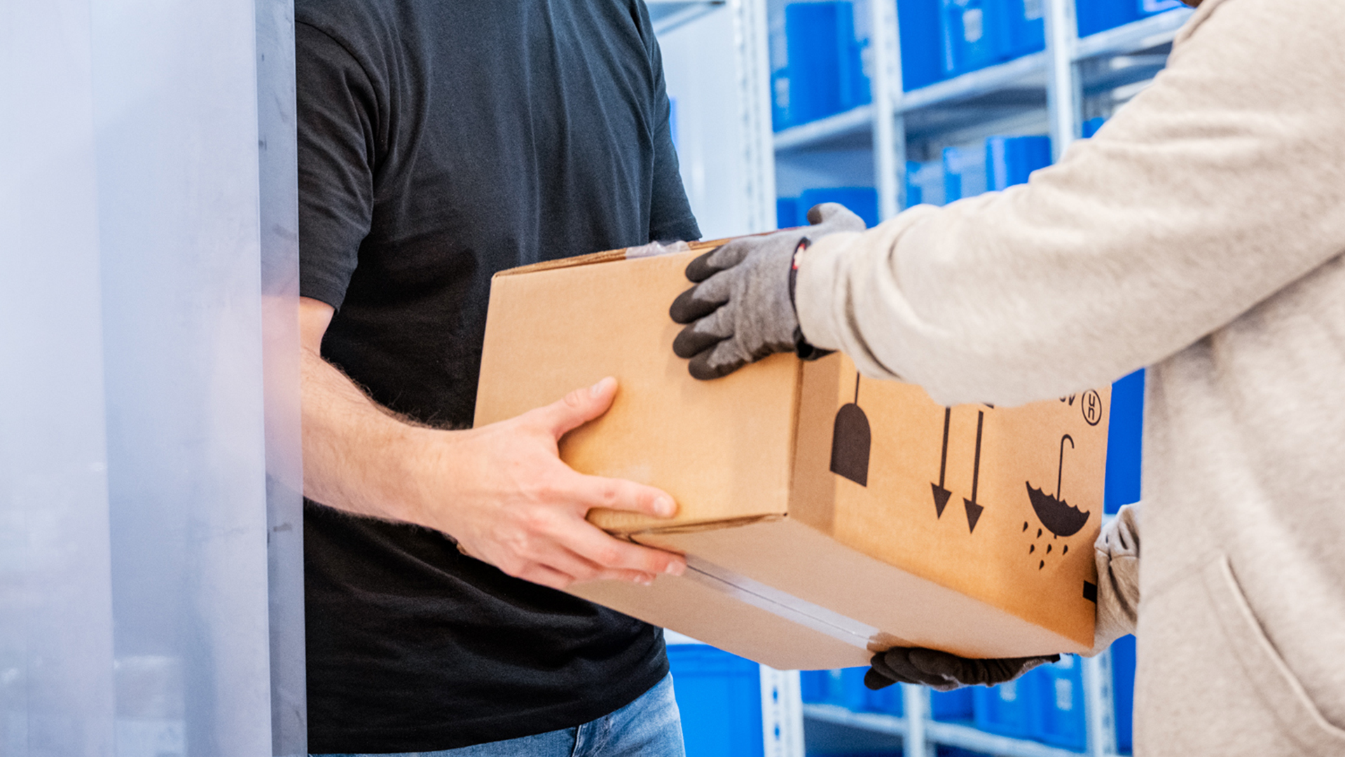 Paketübergabe zwischen zwei Personen im Lager Zwei Personen übergeben sich ein Paket; eine Person trägt Handschuhe