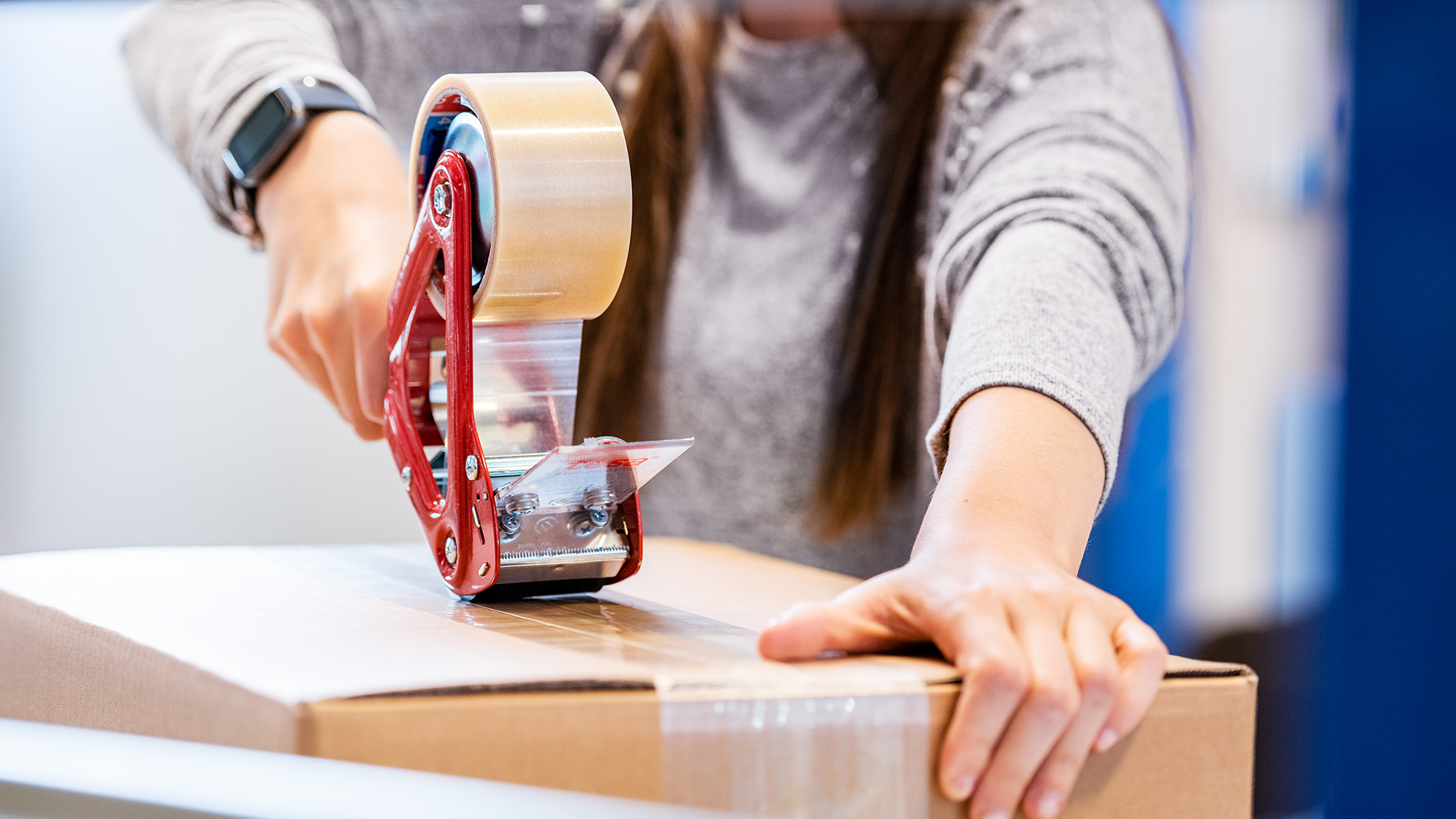 Verpackung eines Pakets mit Klebeband im Lager Eine Person verschließt ein Paket mit einem Handabroller für Klebeband